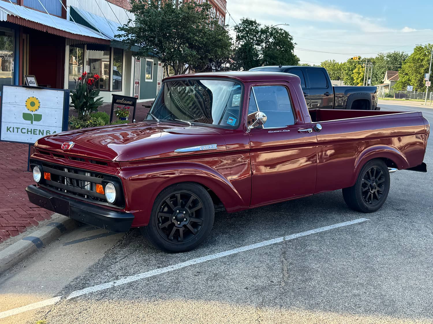 A restored classic pickup parked at the curb beside the Kitchen 64 sidewalk sign on Washington Street