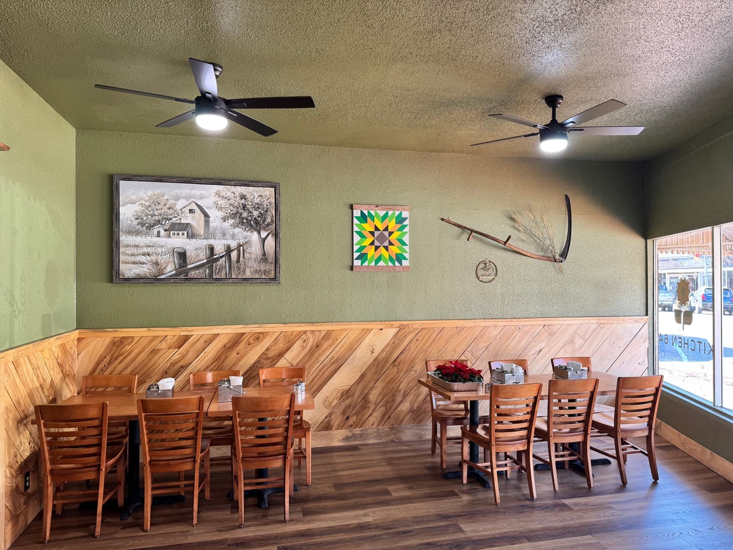 A dining corner at Kitchen 64 with a framed barn painting and a colorful Kansas barn-quilt square