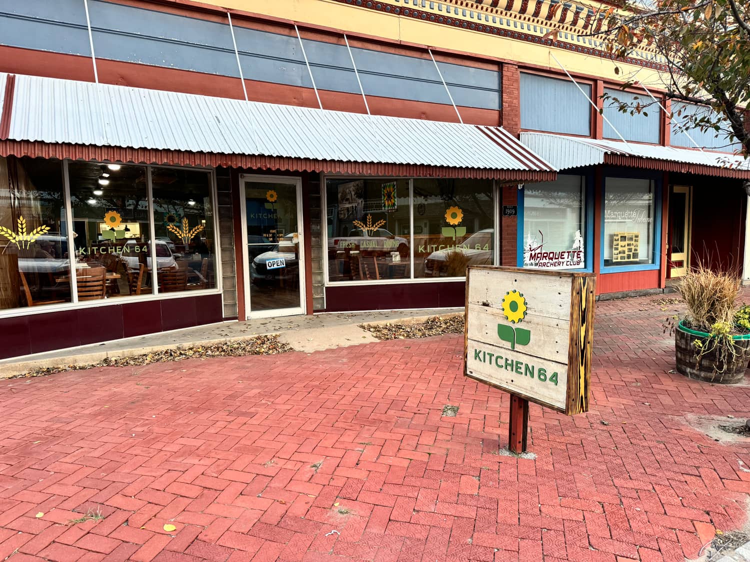 The Kitchen 64 storefront on Washington Street in downtown Marquette, Kansas, with the sidewalk sign out front